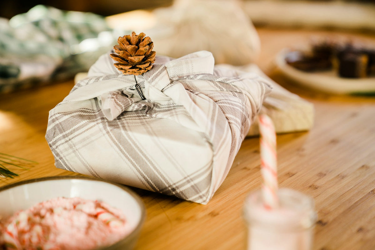 Weihnachtlich verpacktes Geschenk mit Tannenzapfen und Kerze auf einem Holztisch
