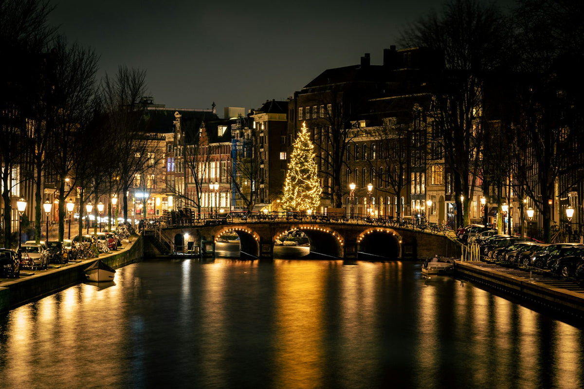 Verlichte kerstboom op een brug over een Amsterdamse gracht bij avond