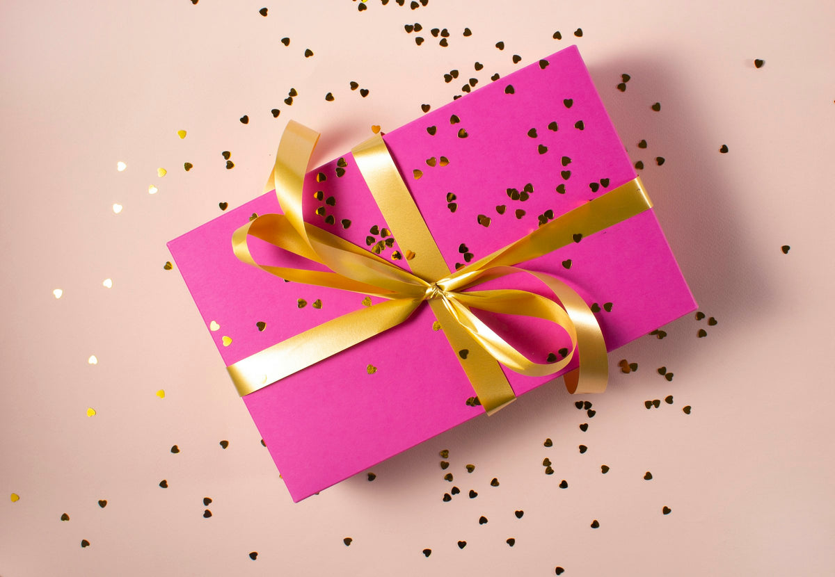 Cadeau emballé dans du papier rose avec un ruban doré et des confettis